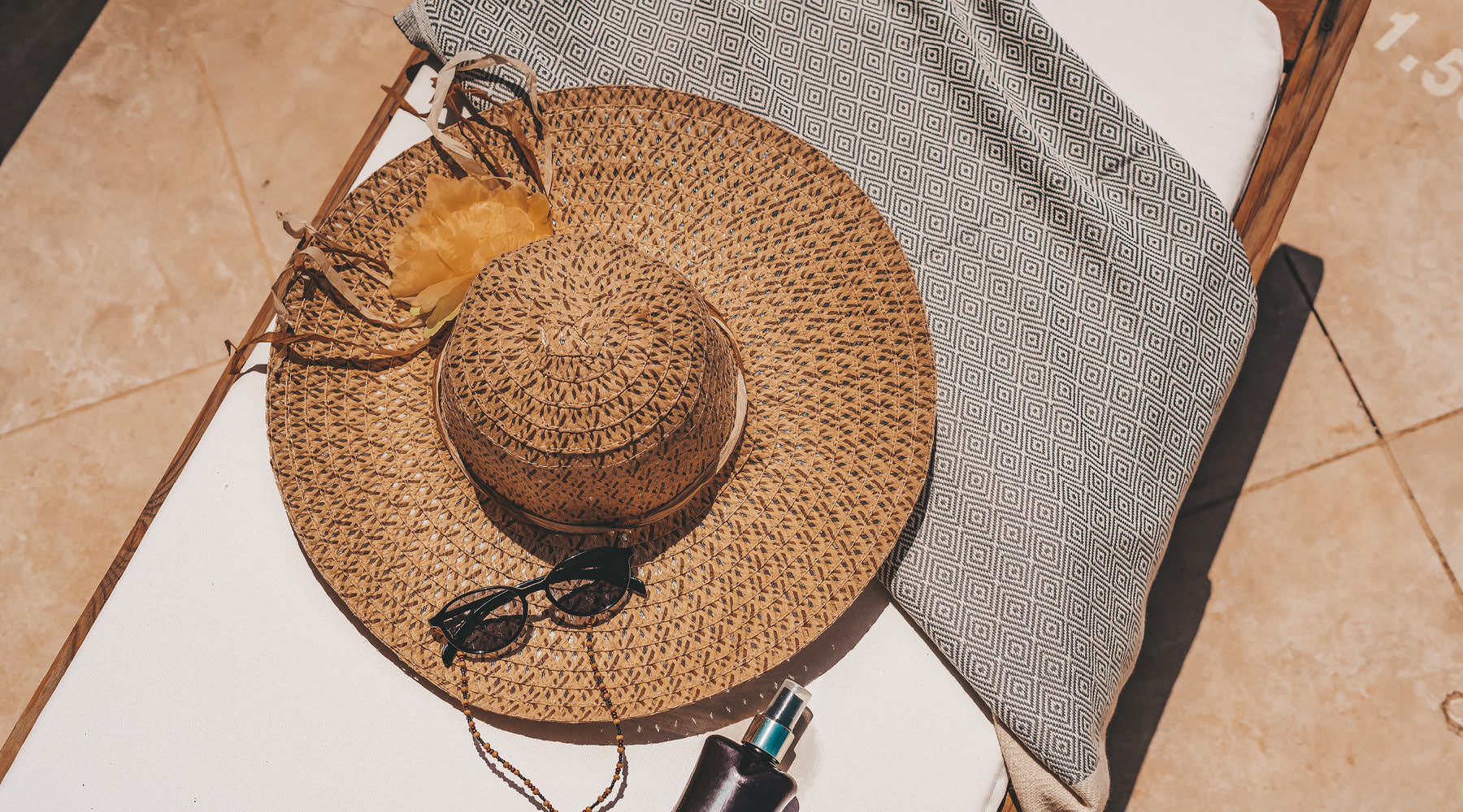 Live Better at ARIZA sun glasses, hat and sunscreen laid out on a lounge chair with a towel