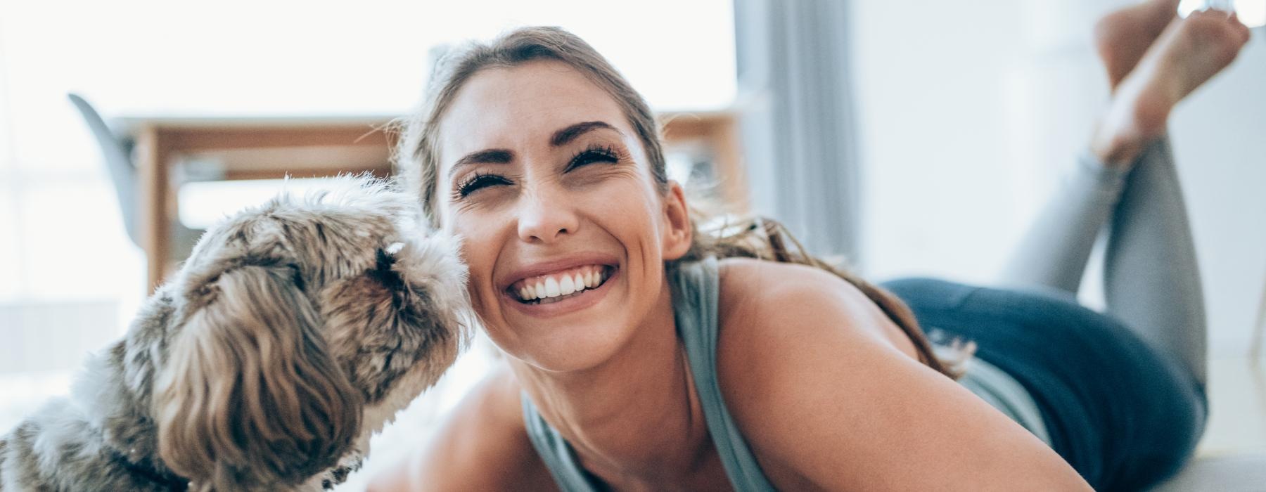 woman smiles as dog kisses her face